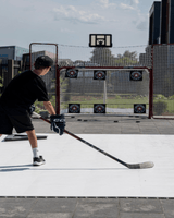 Ung kille övar hockeyskott på ett plastis hockeygolv med mål bakom sig, perfekt för torrlandsträning.