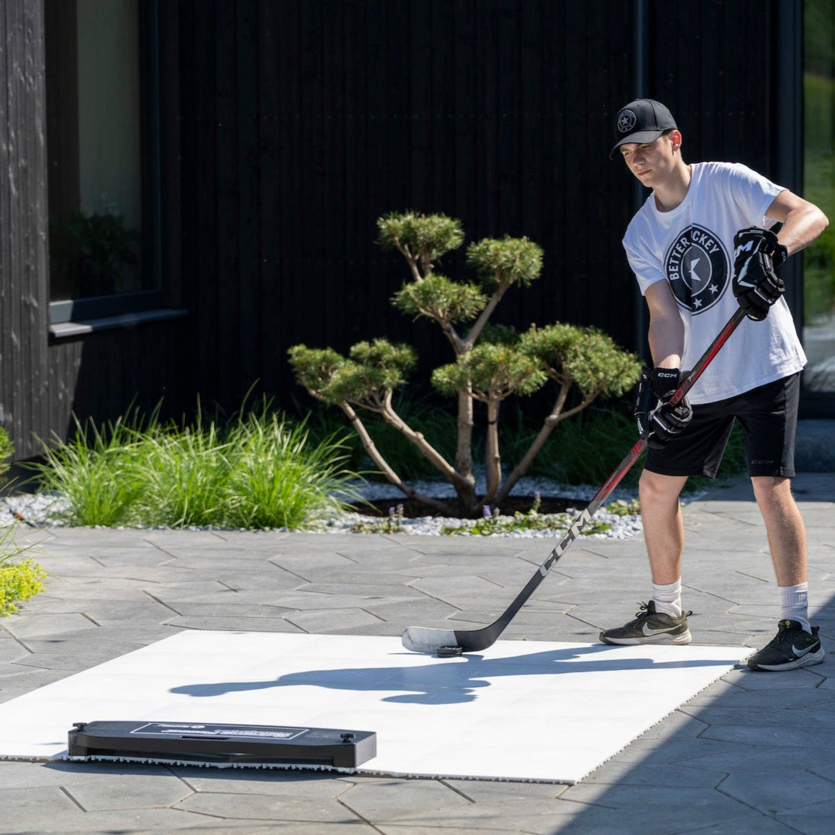 En ung man tränar hockey på ett plastis golv utomhus. Han använder en klubba och puck på Extreme Hockey Flooring Tiles.